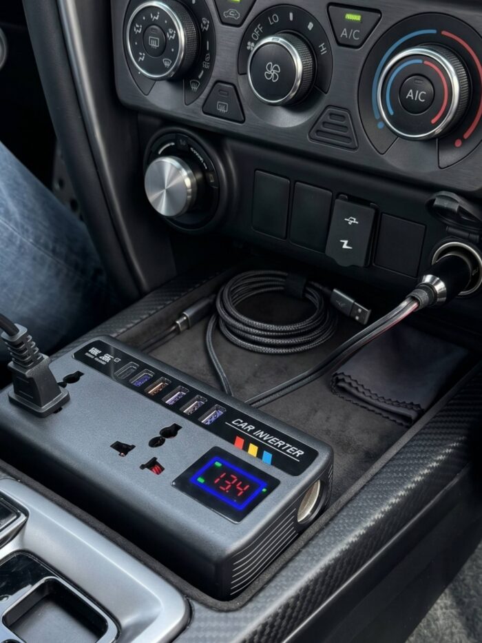Inversor de corriente compacto para auto, mostrando su pantalla digital encendida y conectores USB-C en un tablero minimalista.